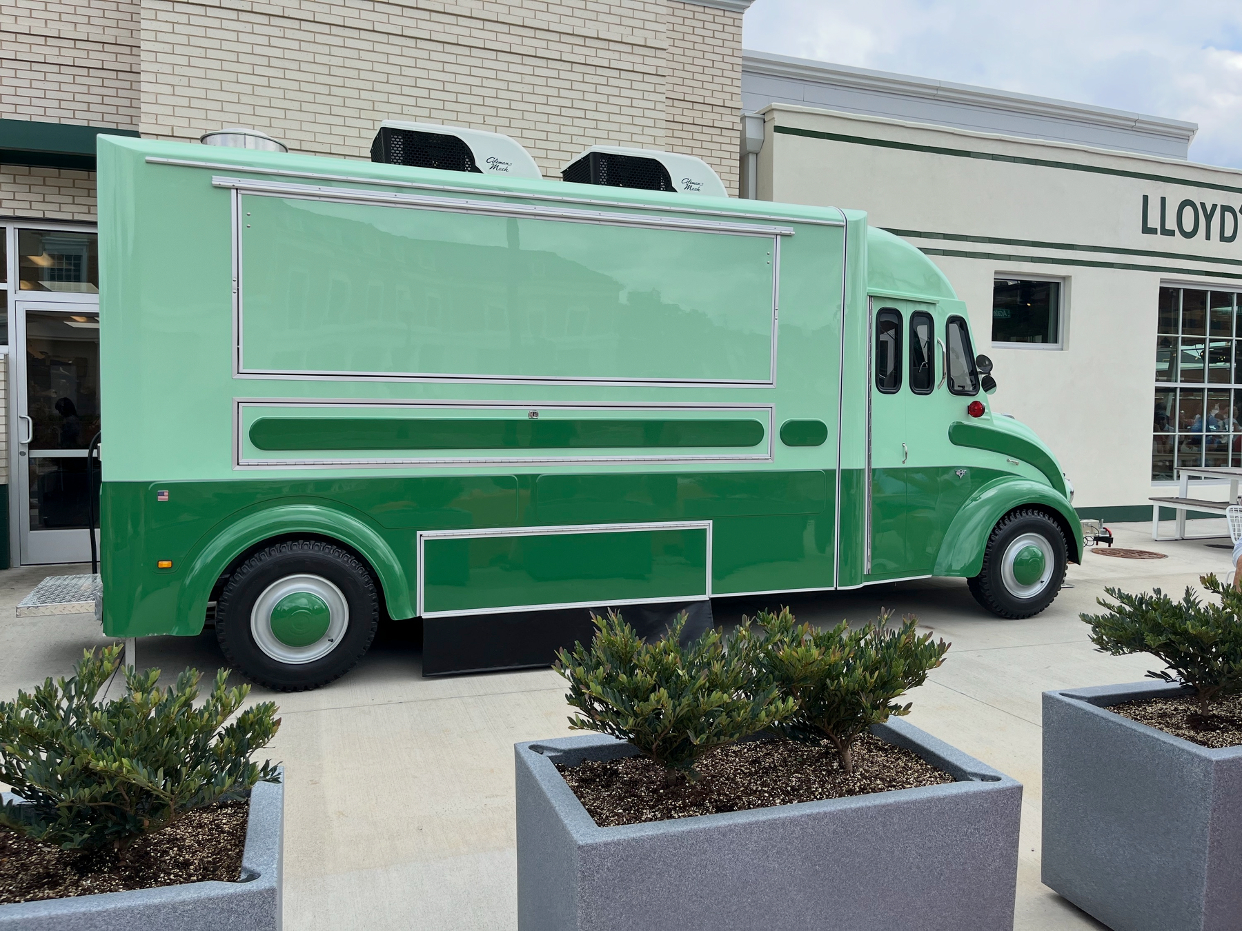 A vintage green delivery truck is parked outside a building with large windows and the name LLOYD visible.